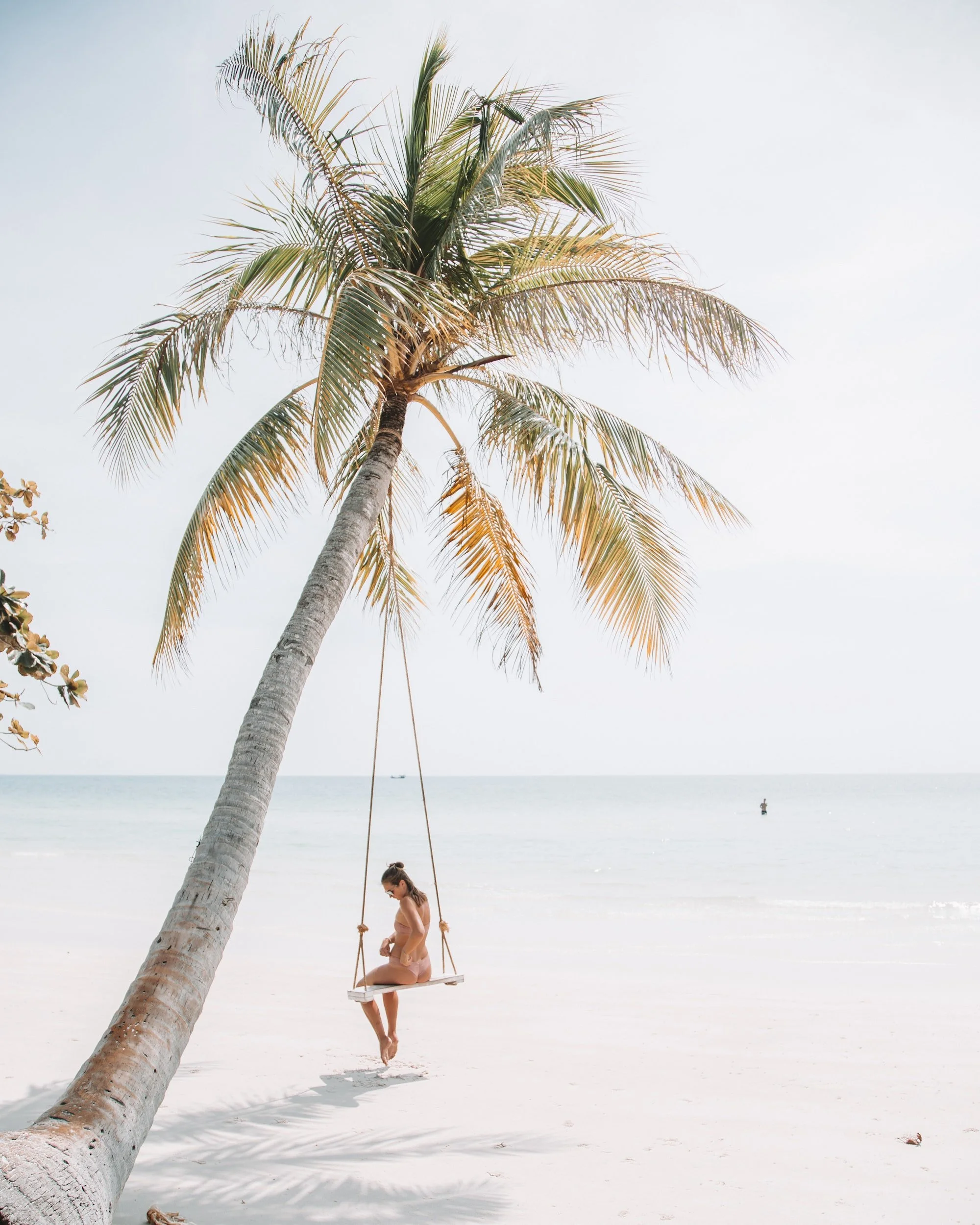 women sits on a swing hanging from a palm tree on her solo trip in tulum, mexico